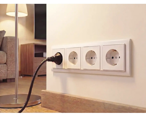 4-voudige wandcontactdoos aan een lichte wand in de woonkamer met een zwarte stekker van een vloerlamp.