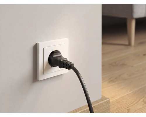 Zwarte randaardestekker in wit stopcontact in een lichte kamer met houten vloer.