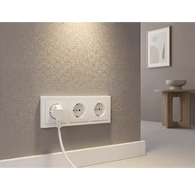 Drievoudige wandcontactdoos met ingestoken stekker op een muur met textuur in een lichte kamer.