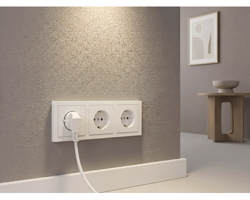 Drievoudige wandcontactdoos met ingestoken stekker op een muur met textuur in een lichte kamer.