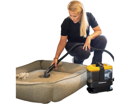 Een vrouw reinigt een grijze hondenmand met een draagbare Powerplus vlekkenreiniger en bekledingsreiniger.