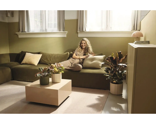 Licht ingerichte woonkamer met groene bank, beige salontafel en diverse kamerplanten in potten.