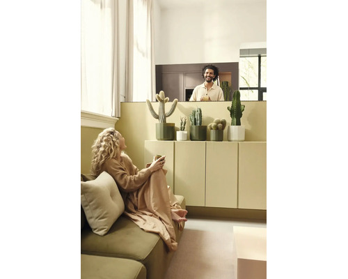 Lichte woonkamer met cactussen in bloempotten op een dressoir, een vrouw op de bank en een lachende man op de achtergrond.