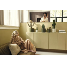 Moderne, lichte woonkamer met cactussen in plantenpotten op een dressoir, een vrouw op de bank en een man op de achtergrond.