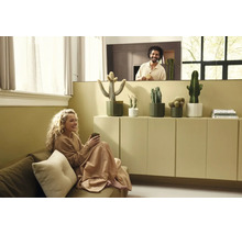 Lichte woonkamer met vrouw op de bank en man achter een wand. Diverse cactussen in potten staan op een minimalistische kast.