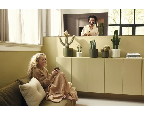 Lichte woonkamer met vrouw op de bank en man achter een wand. Diverse cactussen in potten staan op een minimalistische kast.