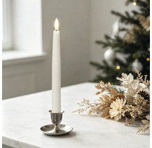 Witte led-tafelkaars in een zilveren houder op een marmeren tafel met feestelijke kerstdecoratie en een wazige kerstboom op de achtergrond.