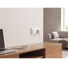 Wandstopcontact met stekker en kabel, aangesloten op een laptop op een houten dressoir in een lichte woonkamer.