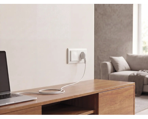 Wandstopcontact met stekker en kabel, aangesloten op een laptop op een houten dressoir in een lichte woonkamer.
