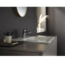 Moderne badkamer met een elegante wastafelkraan op een keramische wastafel, een ronde spiegel en een wastafelmeubel.