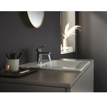 Moderne badkamerkraan met stromend water op een witte wastafel in een donker ingerichte badkamer.