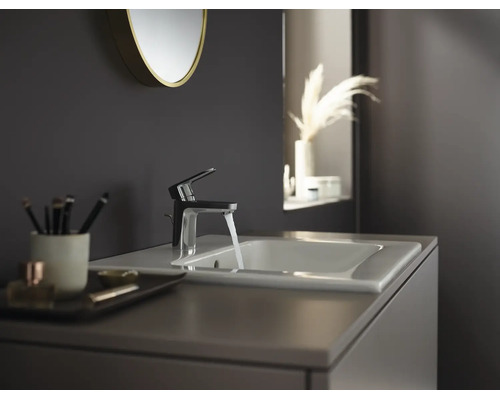Moderne badkamerkraan met stromend water op een witte wastafel in een donker ingerichte badkamer.