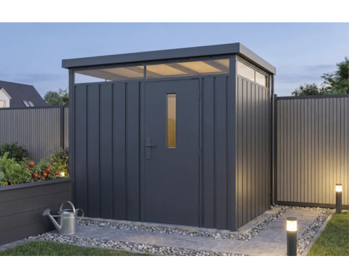 Modern metalen tuinhuis in antraciet met plat dak en lichtkoepels in een verlichte tuin.