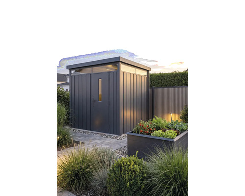 Modern metalen tuinhuis met plat dak en bovenlichten in een aangelegde tuin met een plantenbak en stenen pad.