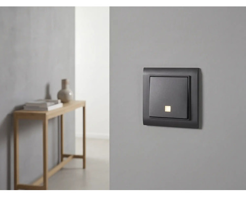 Moderne lichtschakelaar met controlelampje op een grijze muur in een minimalistische kamer.