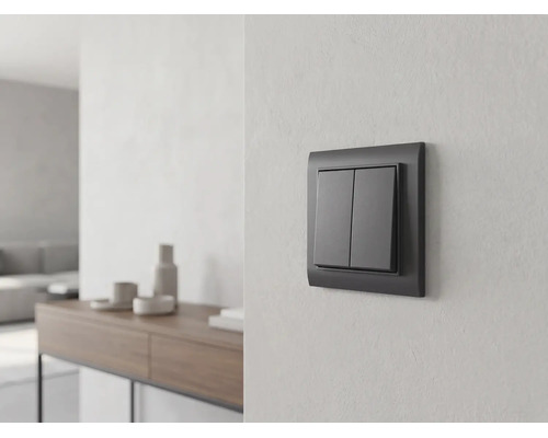 Antracietkleurige serieschakelaar aan een lichte wand in een lichte, modern ingerichte woonkamer met dressoir op de achtergrond.