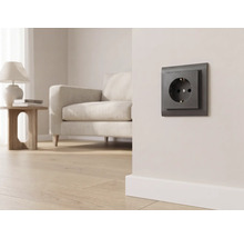 Donker stopcontact op een lichte wand in een modern ingerichte woonkamer met een bank en parketvloer.