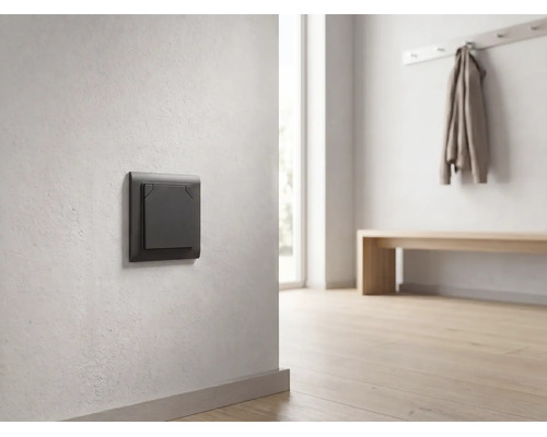 Donkergrijze moderne lichtschakelaar op een lichte muur in een minimalistische, lichte gang met houten vloer.