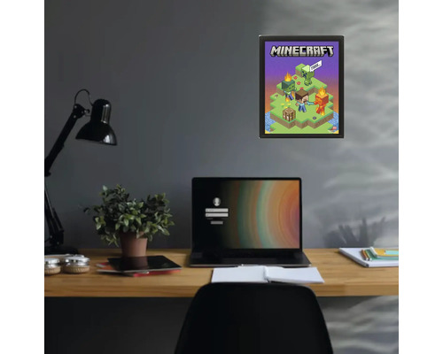 Minecraft poster in een zwarte lijst aan een donkere muur boven een bureau met een laptop en een plant.
