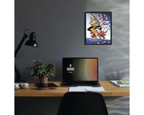Ingelijste One Piece poster aan de muur boven een bureau met laptop en kamerplant.