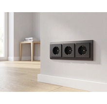 Drievoudig stopcontact in antraciet op een lichte muur in een moderne kamer met houten vloer.