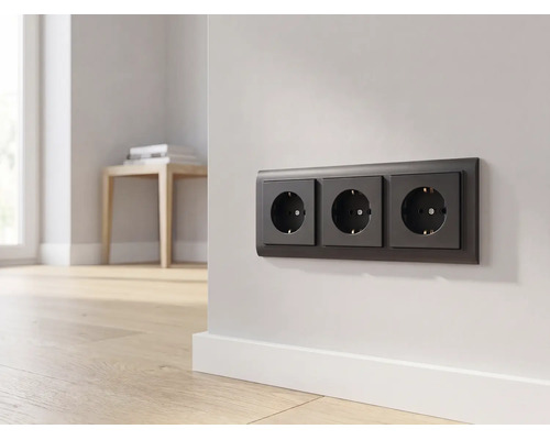 Drievoudig stopcontact in antraciet op een lichte muur in een moderne kamer met houten vloer.