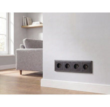 Viervoudig stopcontact in antraciet, gemonteerd op een witte muur in een moderne woonkamer.