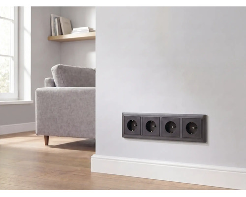 Viervoudig stopcontact in antraciet, gemonteerd op een witte muur in een moderne woonkamer.