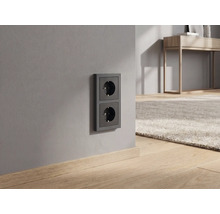Dubbele contactdoos in antraciet op een grijze muur in een modern ingerichte kamer met houten vloer.
