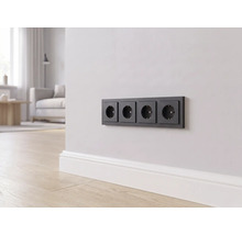 Een 4-voudig stopcontact in zwart aan een lichte wand boven een witte plint in een modern ingerichte woonkamer.