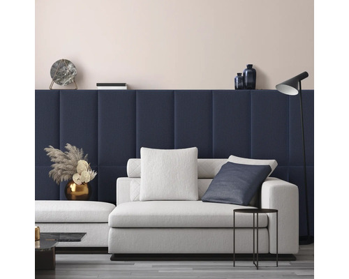 Moderne woonkamer met donkerblauwe gestoffeerde wandpanelen, een lichtgrijze bank met kussens, een zwarte bijzettafel en een vloerlamp.