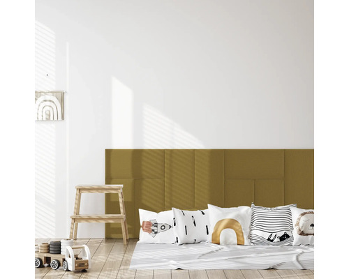 Gestoffeerde wandpanelen in okergeel als hoofdbord in een lichte kinderkamer met sierkussens en houten speelgoed op een lichte houten vloer.