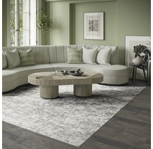 Moderne, lichte woonkamer met een groot grijs-wit gemêleerd vloerkleed, een gebogen crèmekleurige bank en een houten salontafel.