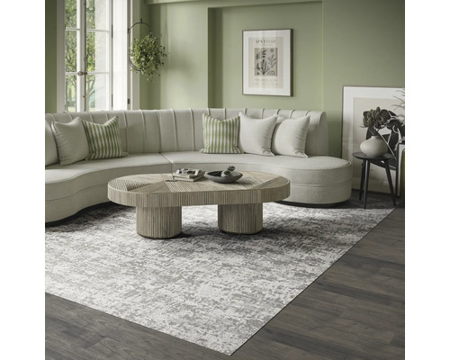 Moderne, lichte woonkamer met een groot grijs-wit gemêleerd vloerkleed, een gebogen crèmekleurige bank en een houten salontafel.