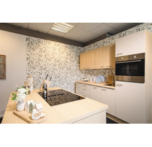 Moderne, lichte keuken met kookeiland voorzien van een zwarte kookplaat, licht houten bovenkasten, witte onderkasten en behang met bloemen.