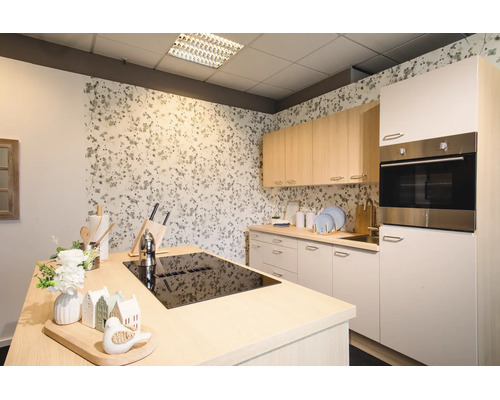 Moderne, lichte keuken met kookeiland voorzien van een zwarte kookplaat, licht houten bovenkasten, witte onderkasten en behang met bloemen.