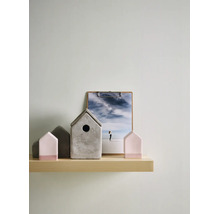 Decoratieve opstelling op een licht houten wandplank met een grijs betonnen vogelhuisje en roze en grijze huisjes in minimalistisch design.