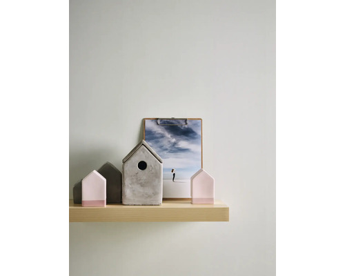 Decoratieve opstelling op een licht houten wandplank met een grijs betonnen vogelhuisje en roze en grijze huisjes in minimalistisch design.