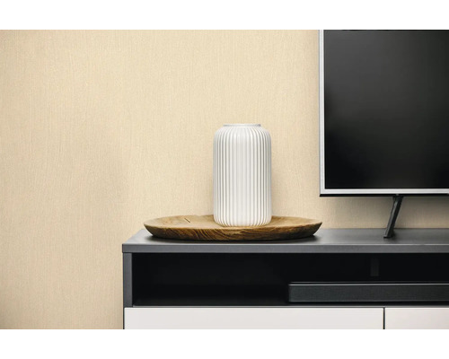 Gestructureerd behang in beige achter een donker dressoir met een witte vaas en een televisie.