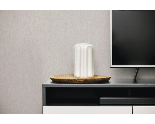 Gestructureerd vliesbehang in een moderne woonkamer achter een tv-meubel met een witte vaas op een houten dienblad.