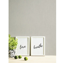 Gestructureerd behang met verticale nerf in een lichte, neutrale tint, gecombineerd met witte fotolijsten en een groene plant.