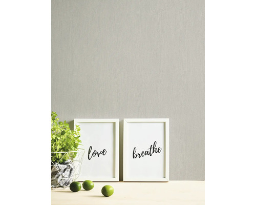 Gestructureerd behang met verticale nerf in een lichte, neutrale tint, gecombineerd met witte fotolijsten en een groene plant.