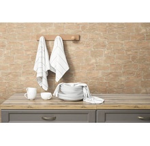 Vliesbehang met steenlook op een keukenwand met servies en theedoeken op een houten aanrechtblad.