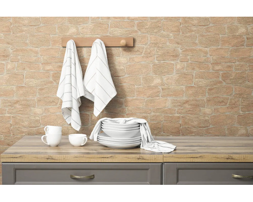 Vliesbehang met steenlook op een keukenwand met servies en theedoeken op een houten aanrechtblad.