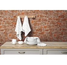 Behang met baksteenmotief op een keukenmuur achter wit servies en keukendoeken op een houten blad.