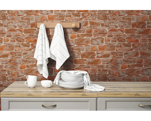 Behang met baksteenmotief op een keukenmuur achter wit servies en keukendoeken op een houten blad.