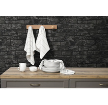 Moderne keuken met donkere muur in steenlook, houten werkblad, wit servies, gestreepte doeken aan een rek en grijze keukenkastjes.
