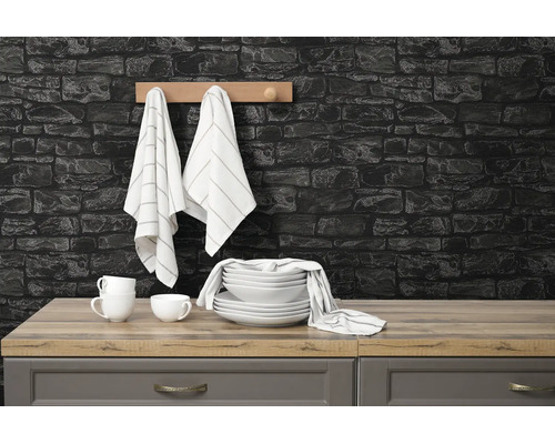 Moderne keuken met donkere muur in steenlook, houten werkblad, wit servies, gestreepte doeken aan een rek en grijze keukenkastjes.