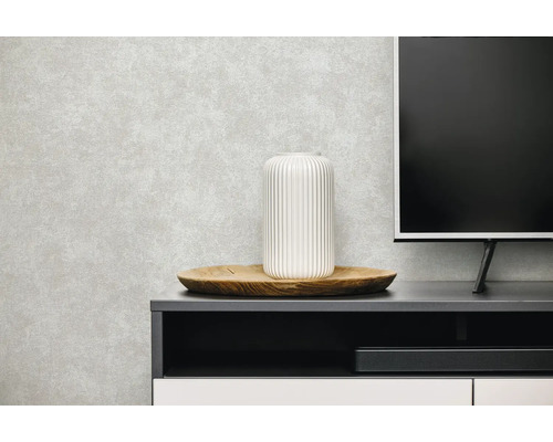 Lichtgrijs vliesbehang met betonlook textuur in een moderne woonkamer achter een tv-meubel met houten dienblad en witte vaas.