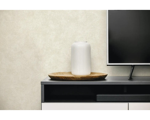 Gestructureerd behang in licht beige, geplaatst achter een tv-meubel met een vaas en houten dienblad in een lichte woonkamer.